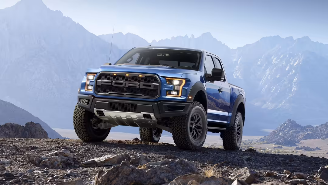 Blue off-road pickup truck parked on rocky terrain with dramatic snow-capped mountain peaks and valley landscape in bright da