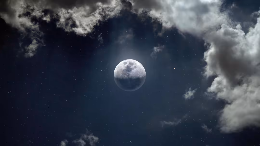 Full moon glowing brightly surrounded by dramatic white clouds against a dark starry night sky with scattered stars visible t