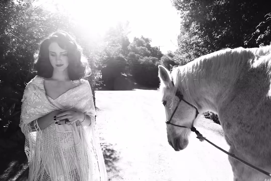 Black and white vintage portrait of a woman in an elegant white dress standing beside a horse in a tree-lined setting with so