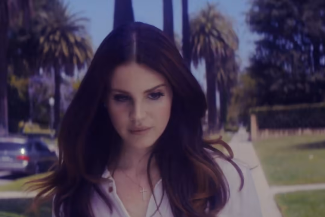 Woman with long dark hair standing among palm trees with a contemplative expression, filtered with vintage color tones