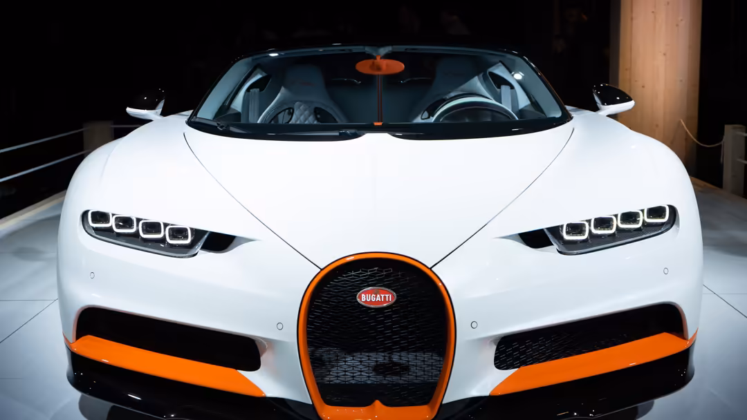 White Bugatti Chiron Sport with distinctive orange accents, featuring sleek LED headlights and iconic oval grille in modern g