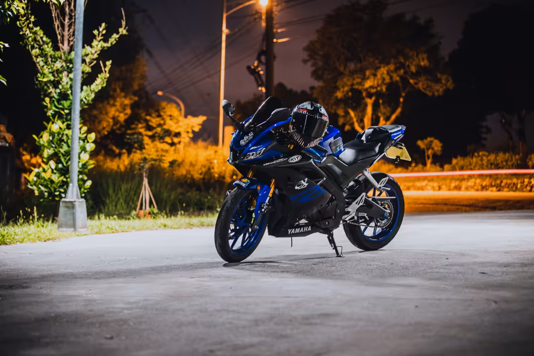 Blue and black sport motorcycle parked on street at night with street lights and trees illuminated in warm golden tones in ba